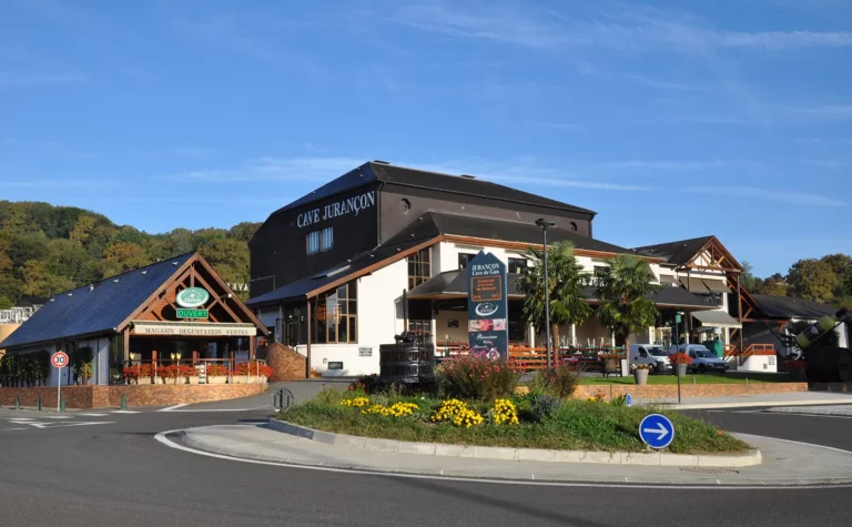 Façade de la Cave de Jurançon à Gan par une journée ensoleillée, avec l’espace boutique et les massifs fleuris.
